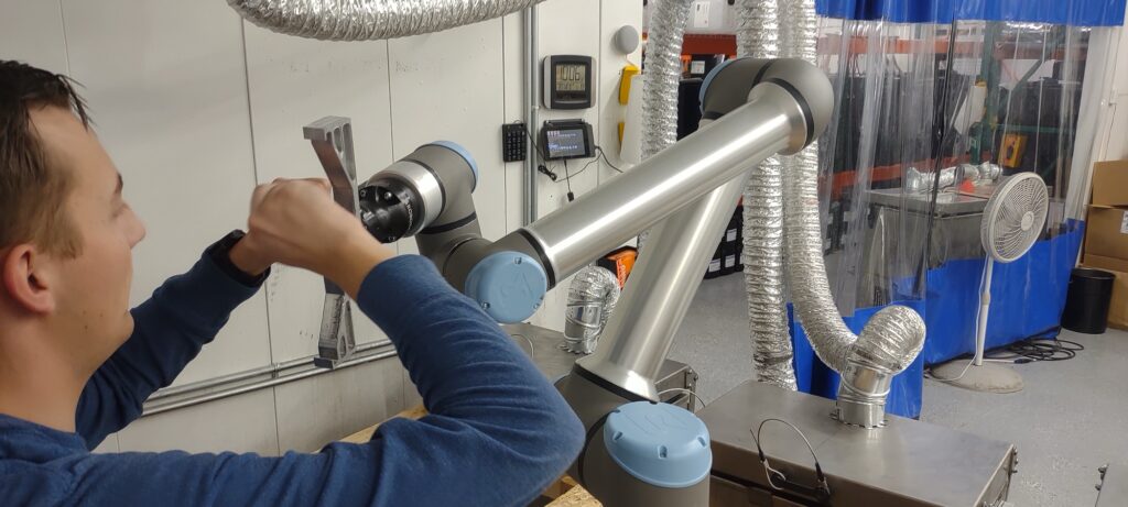 An engineer works with a UR collaborative robot arm on the Merit3D production floor in Price, Utah, automating part handling.