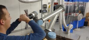 An engineer works with a UR collaborative robot arm on the Merit3D production floor in Price, Utah, automating part handling.
